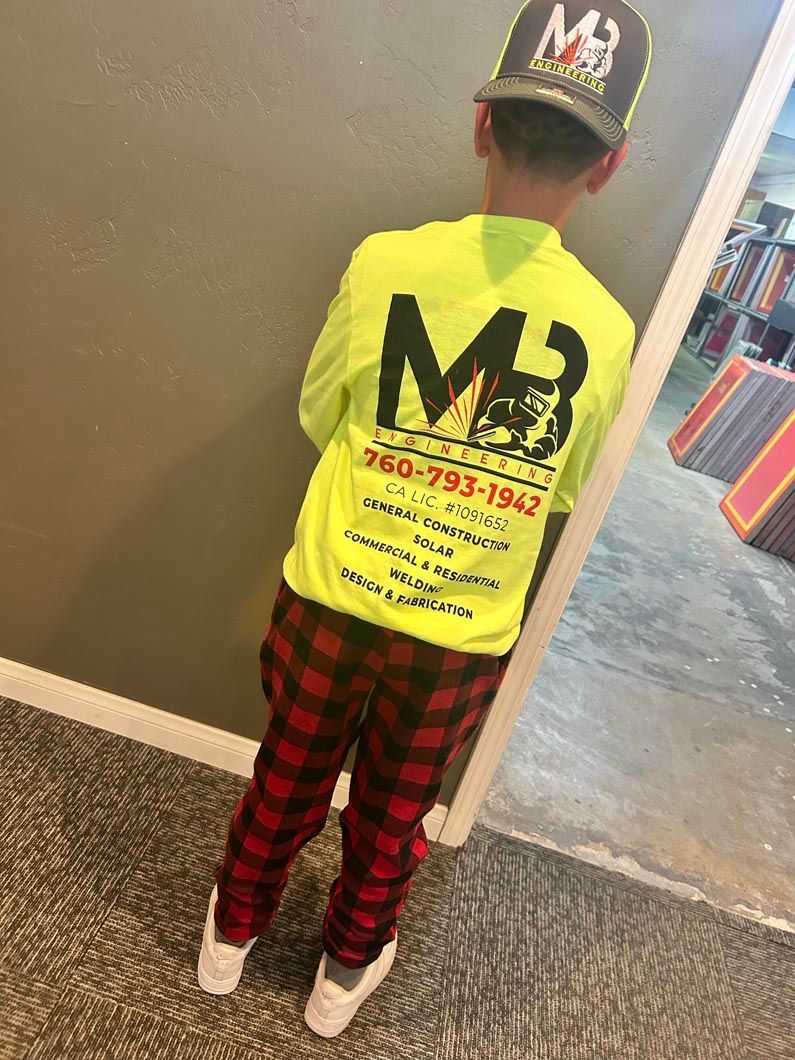 A young boy wearing a yellow shirt and plaid pants is standing next to a door.