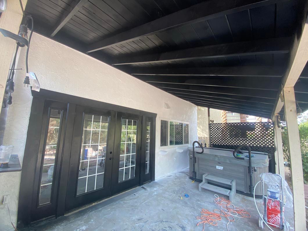 A patio with a black roof and sliding glass doors.