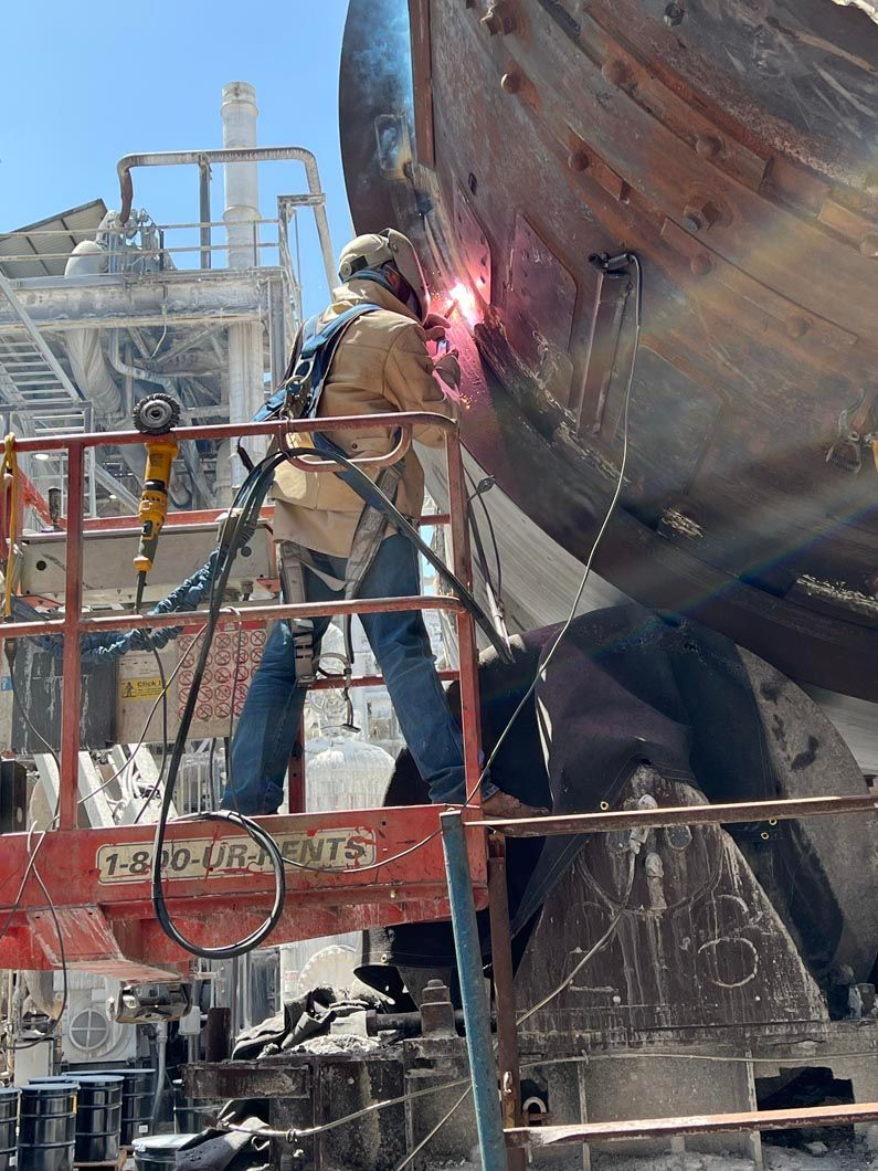 A man is welding a large piece of metal in a factory