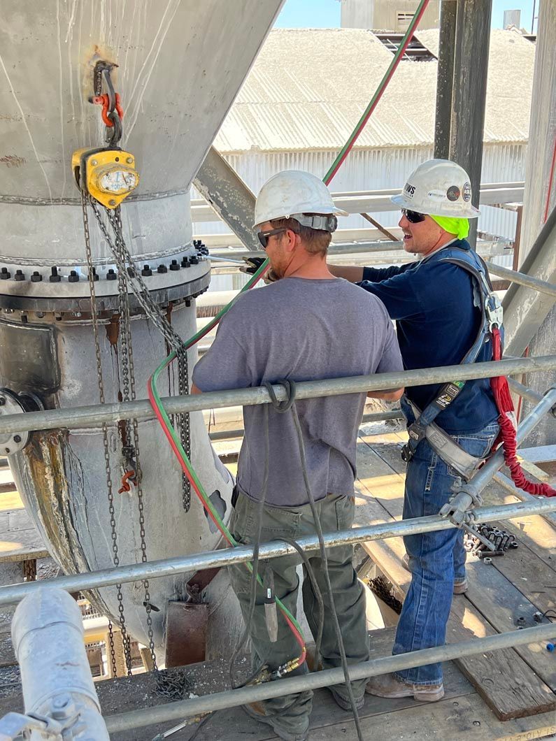 Two men are working on a pipe on top of a building.
