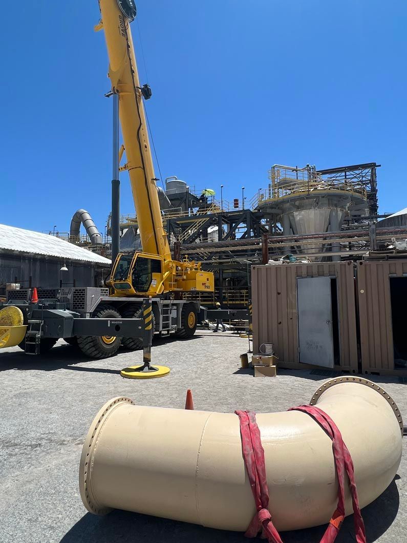A yellow crane is lifting a large pipe in a parking lot.