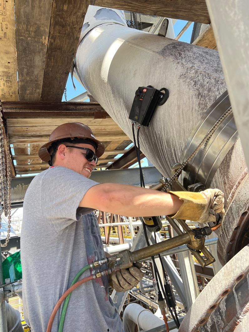 A man wearing a hard hat and sunglasses is working on a pipe.