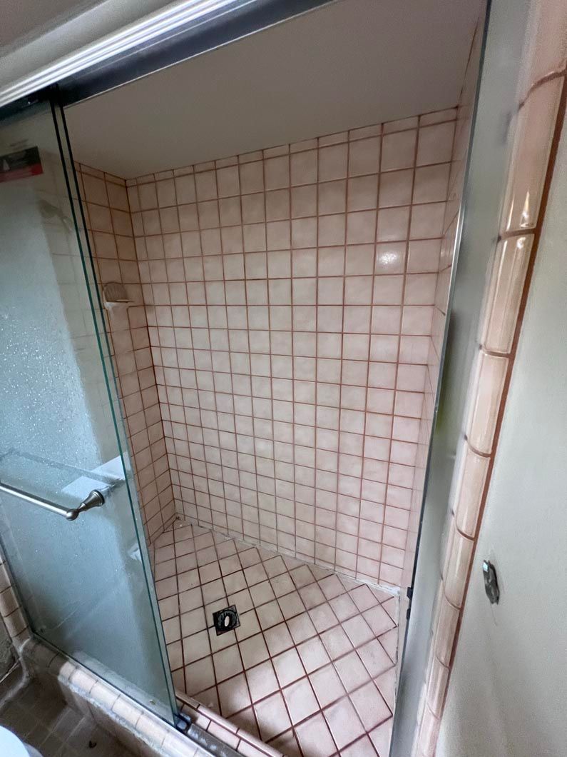 A bathroom with pink tiles and a glass shower door.