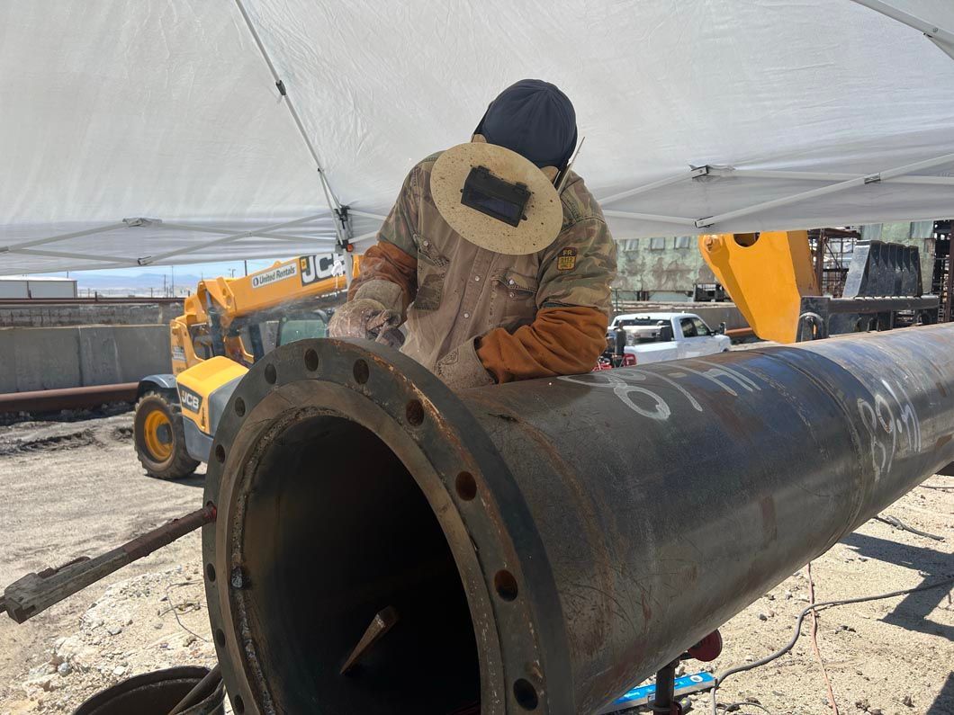 A man is welding a large pipe on a construction site.