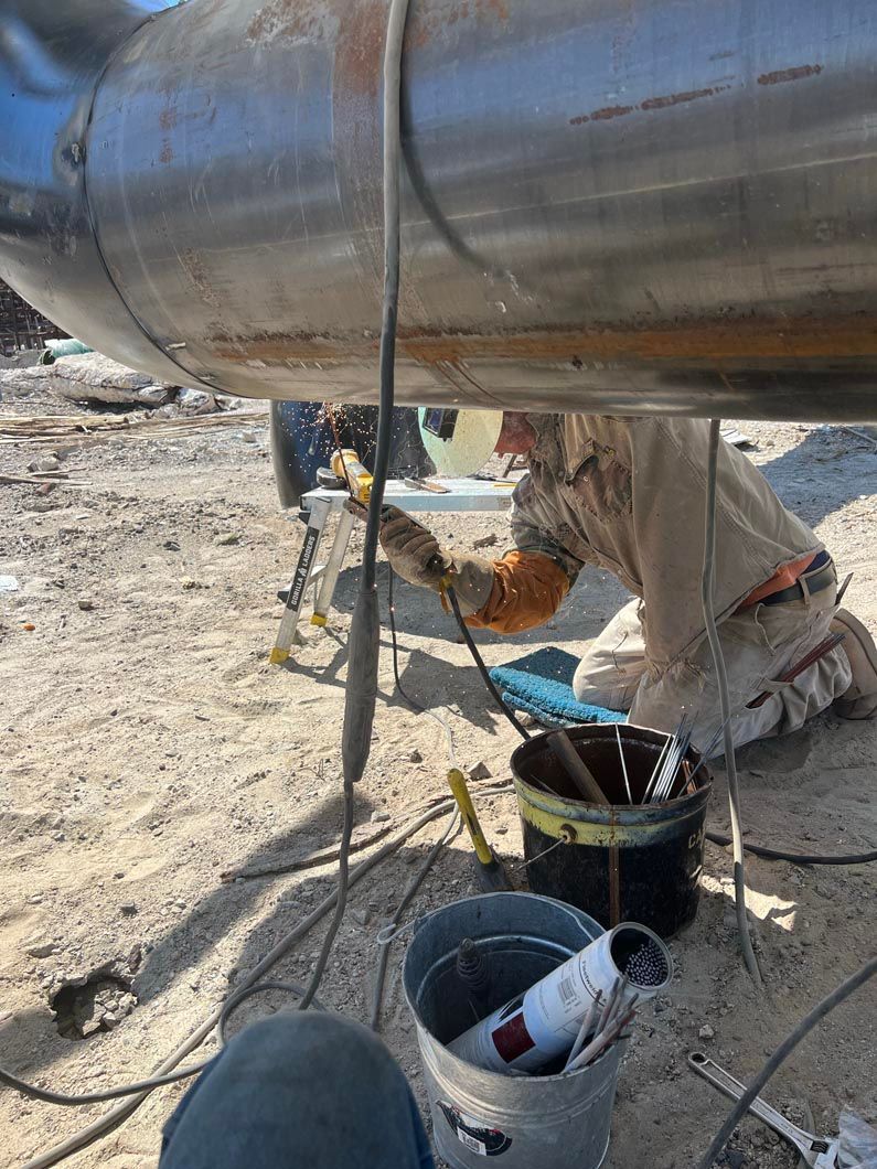A man is welding a pipe in the dirt.
