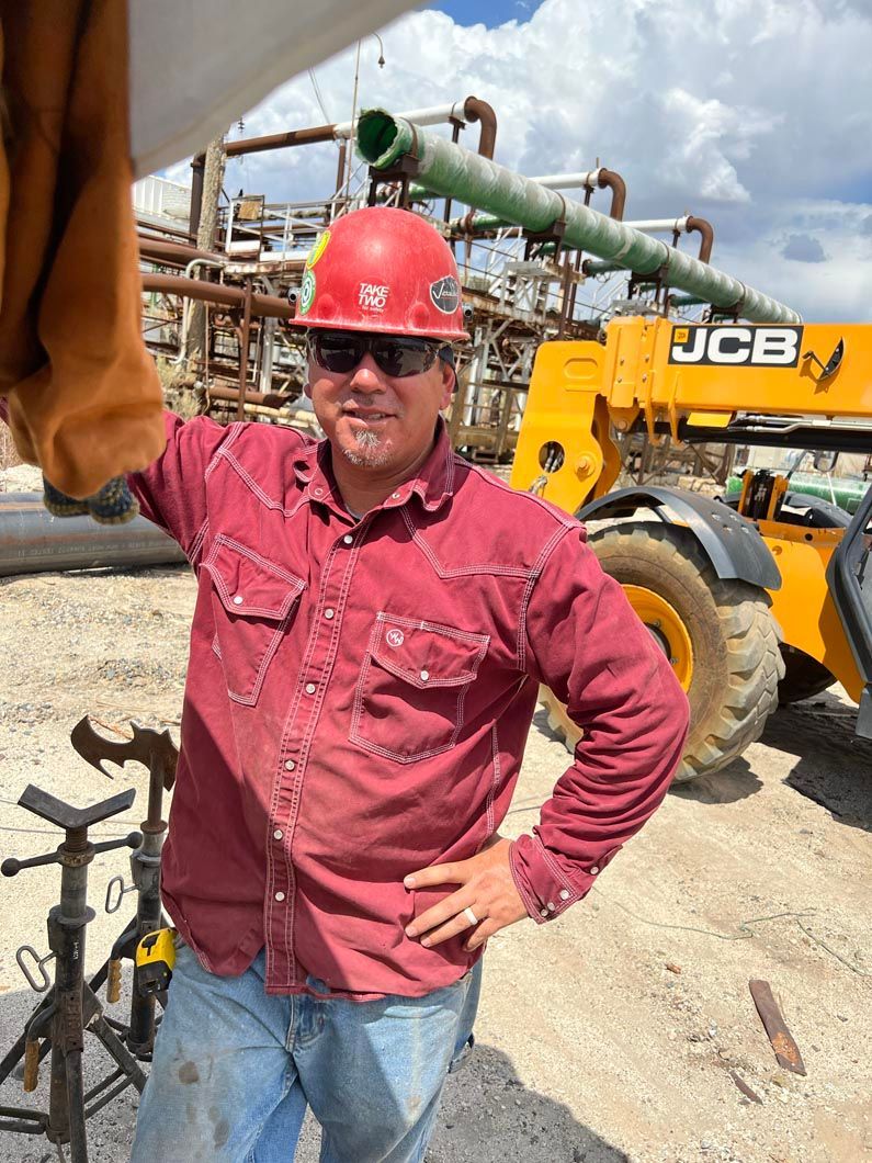 A man wearing a hard hat and sunglasses is standing in front of a jcb tractor.