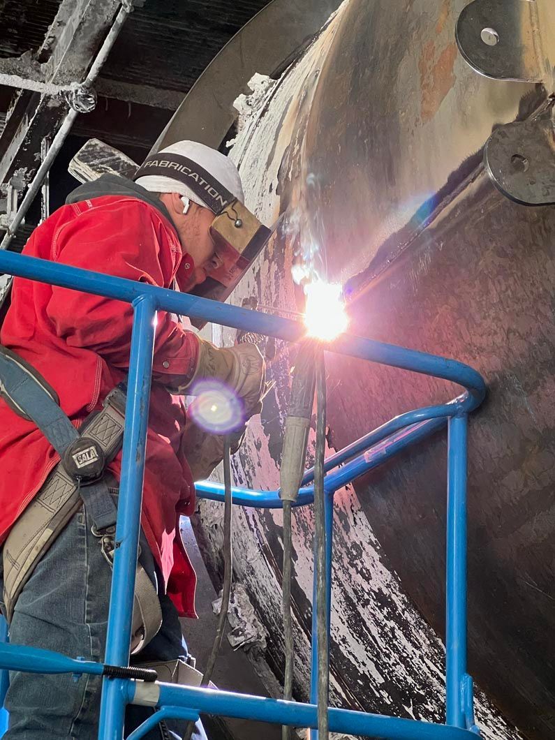 A man in a red jacket is welding a pipe