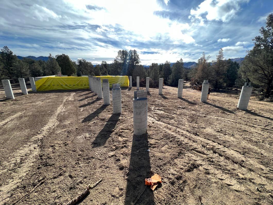 A row of concrete poles in a dirt field with trees in the background