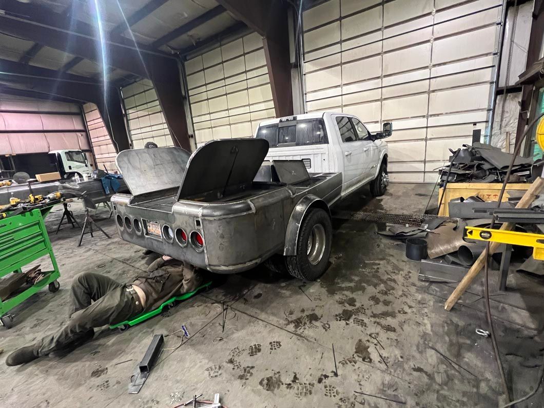 A man is laying on the ground under a truck in a garage.