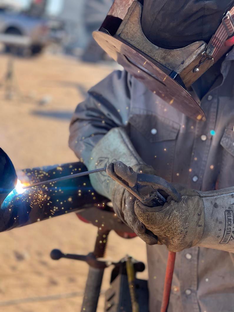 A man wearing a mask and gloves is welding a pipe.