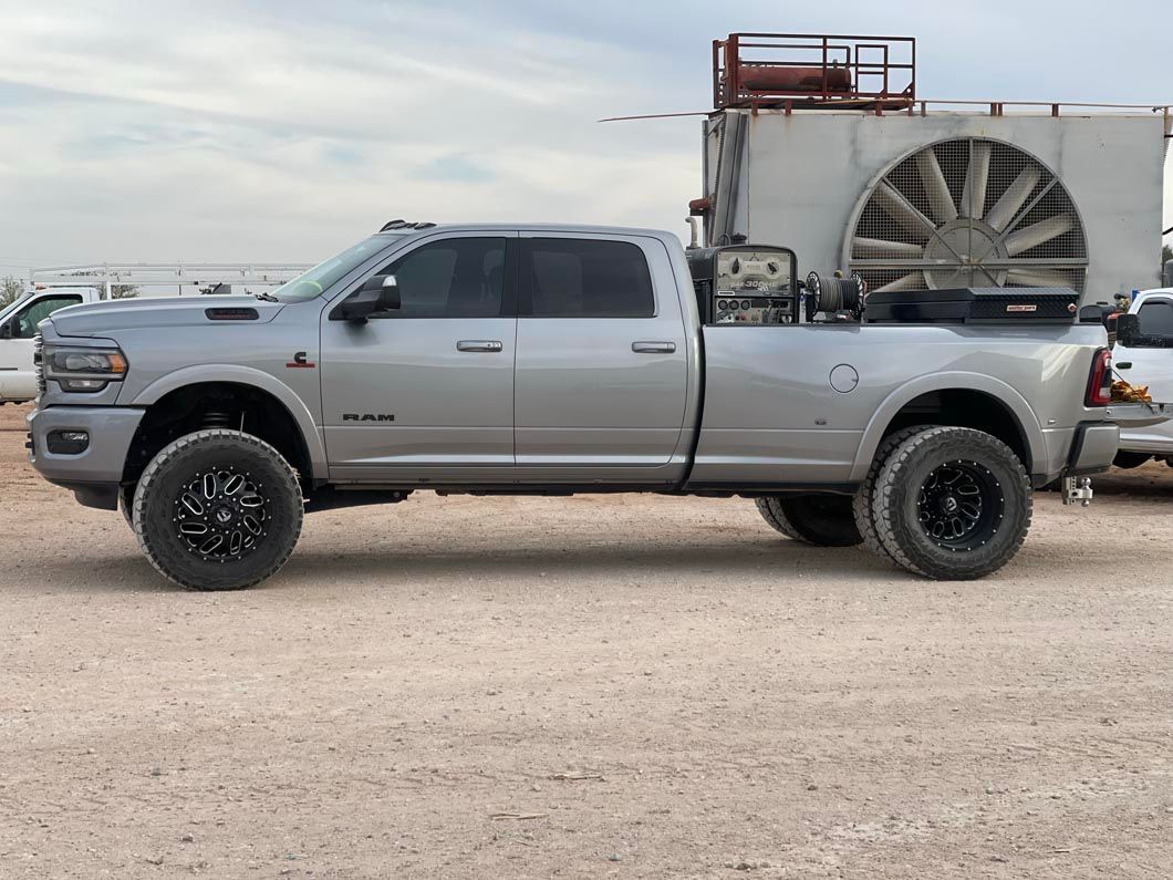 A silver truck with a fan attached to the back is parked in a gravel lot.