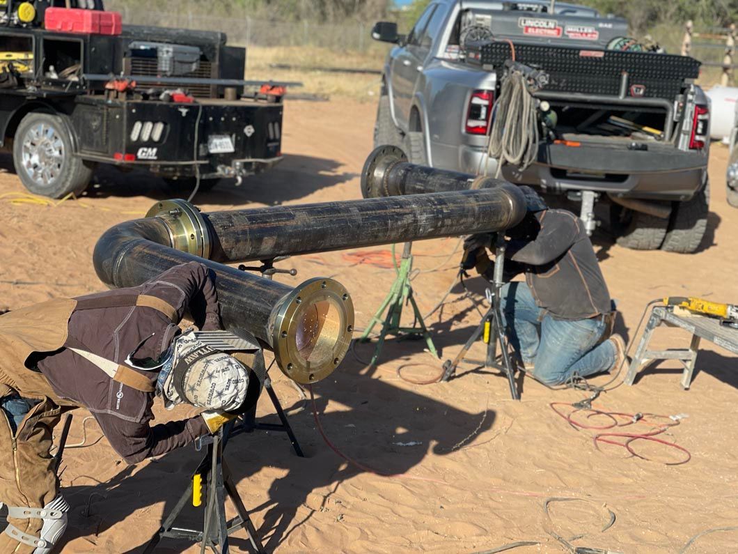 A man is welding a pipe in the dirt in front of a truck.