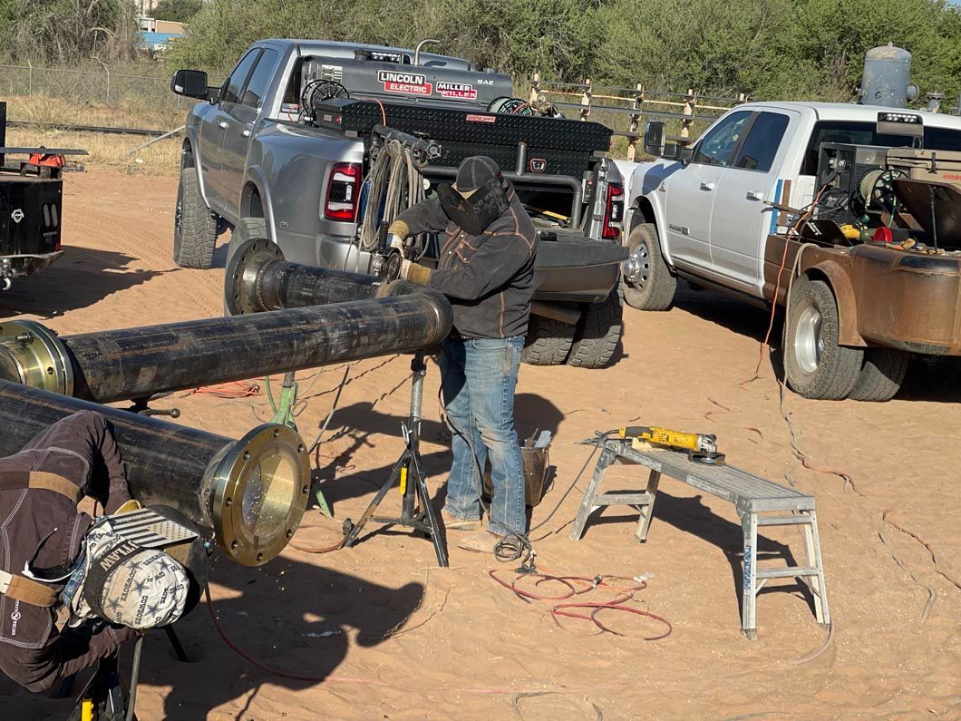 A man is welding a pipe in a field next to a truck.