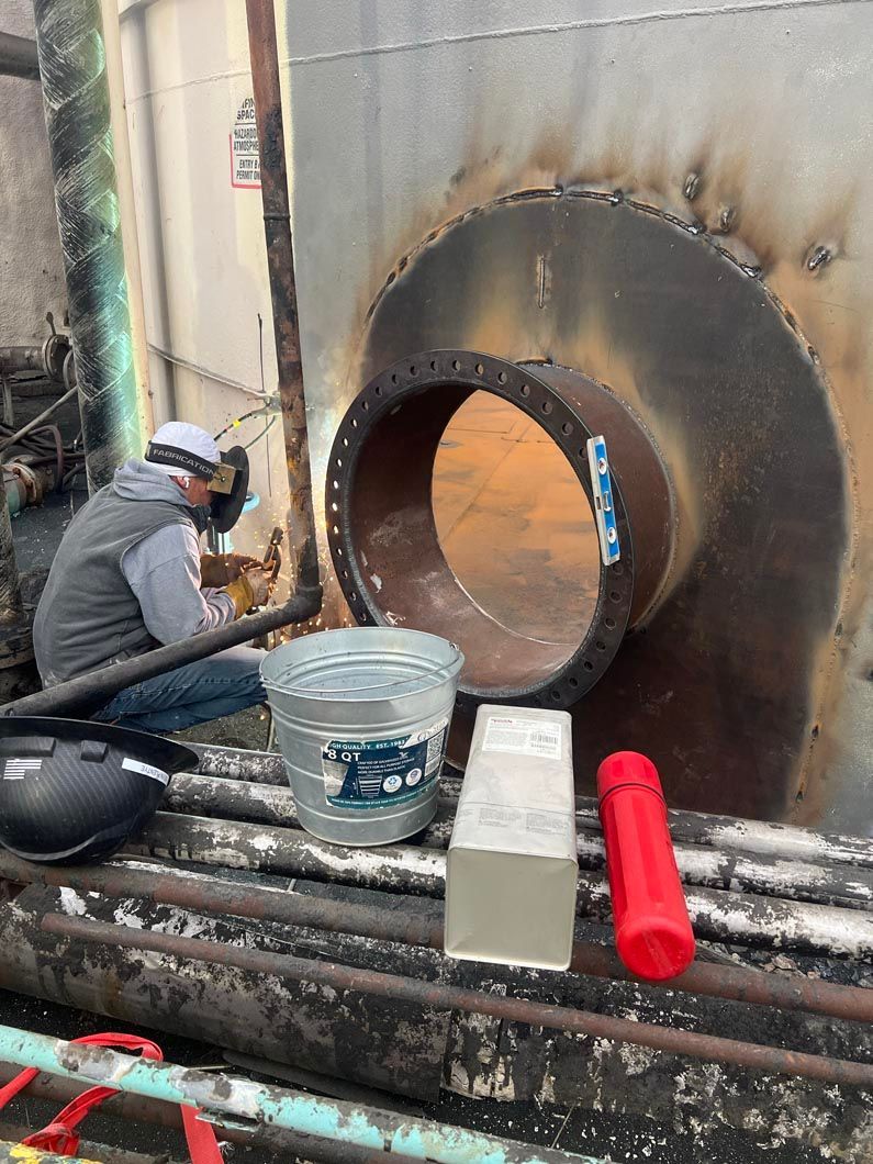 A man is welding a large pipe in a factory.