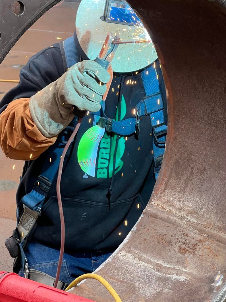 A man wearing a shirt that says ' burton ' on it is welding a pipe.