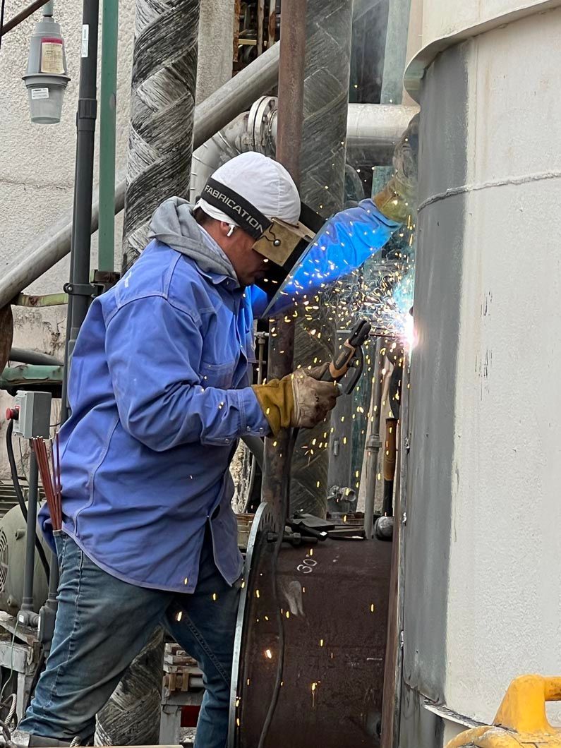 A man in a blue shirt is welding a pipe.