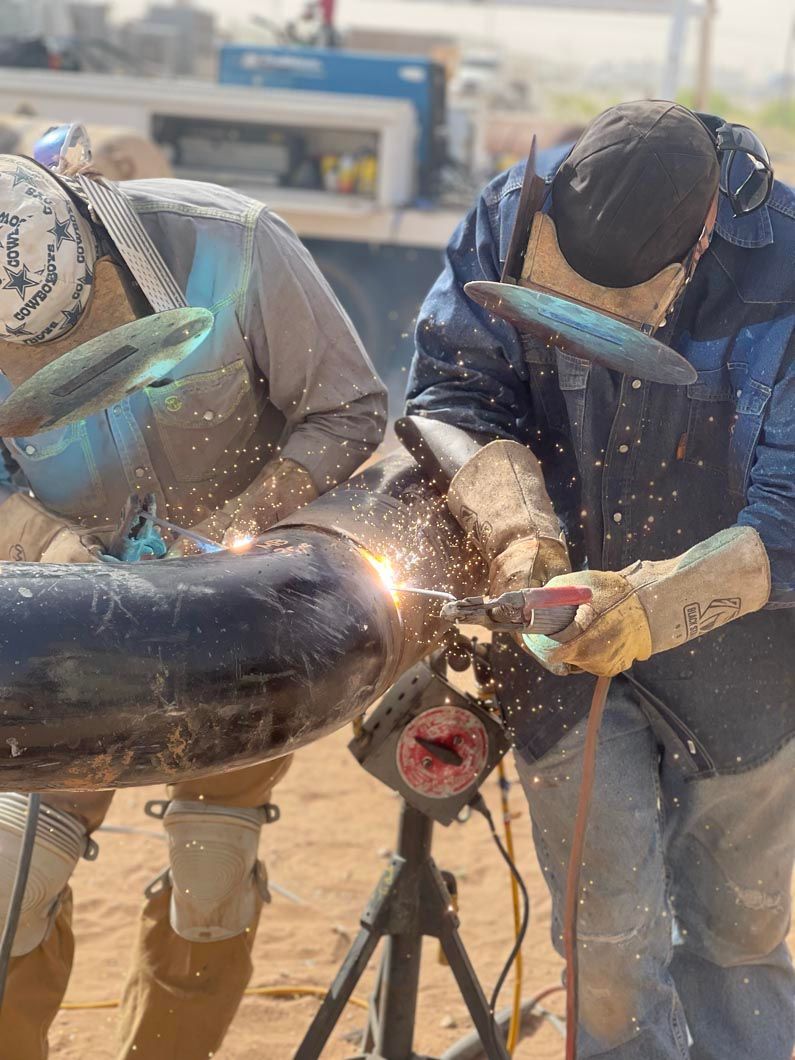 Two men are welding a pipe together in the desert.