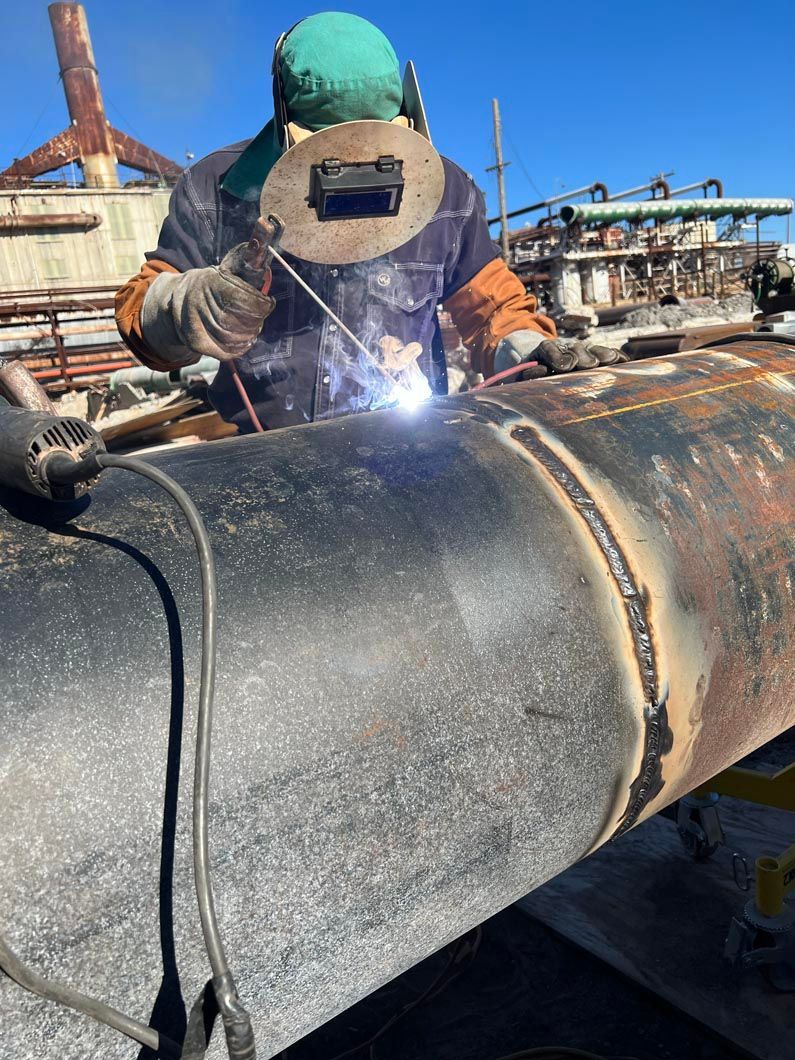 A man is welding a large pipe in a factory.