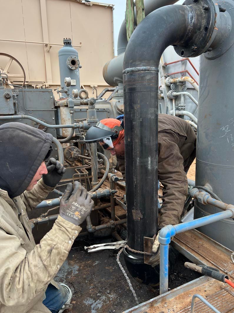 Two men are working on a pipe in a factory.