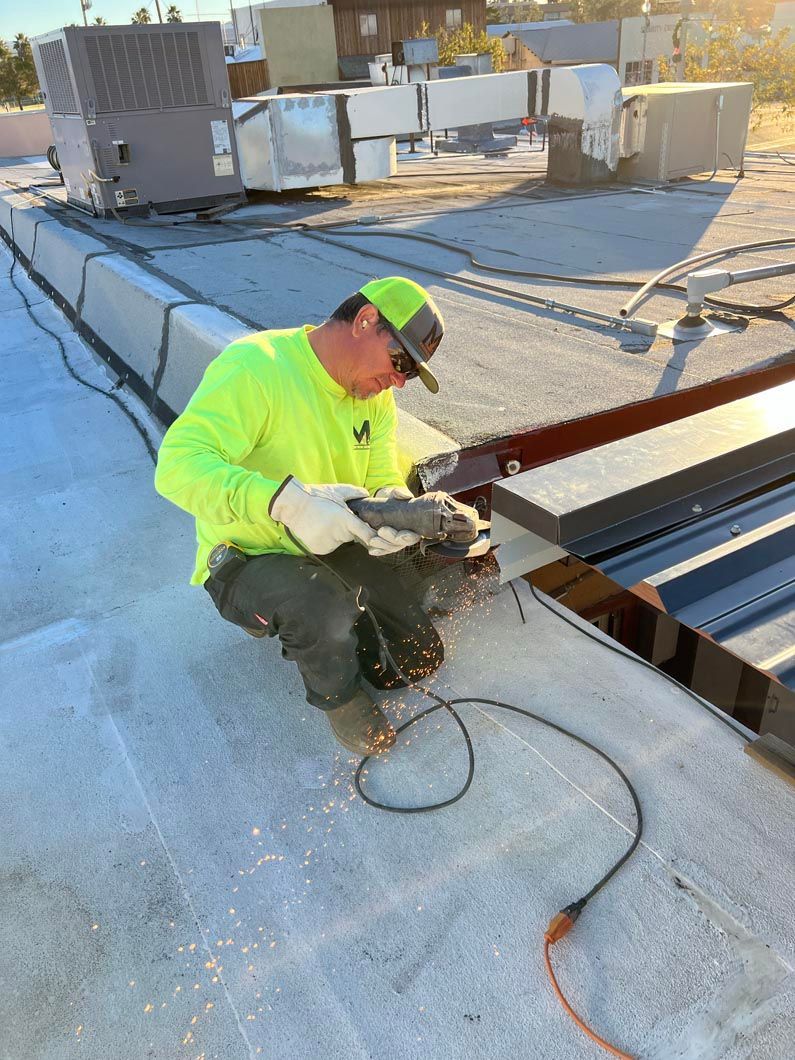 A man is kneeling down on a roof using a grinder.