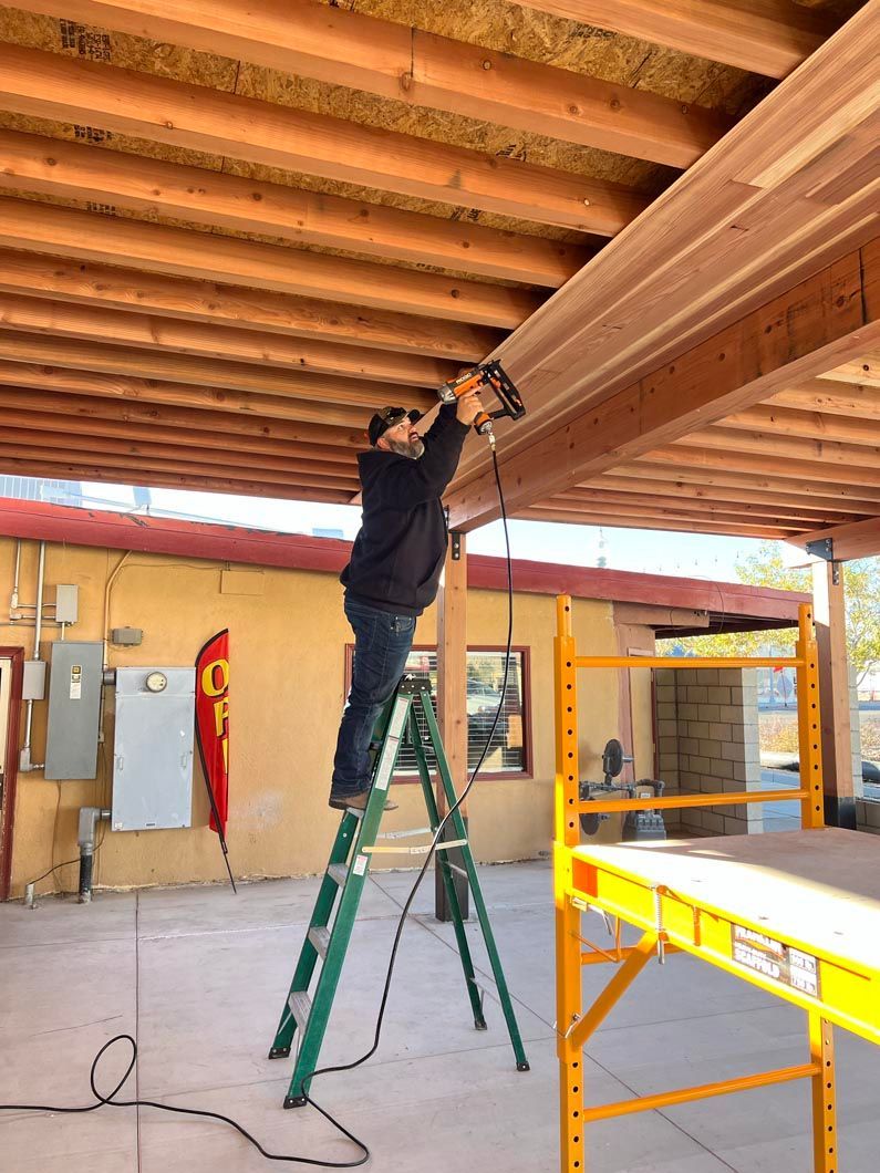 A man is standing on a ladder working on a wooden ceiling.