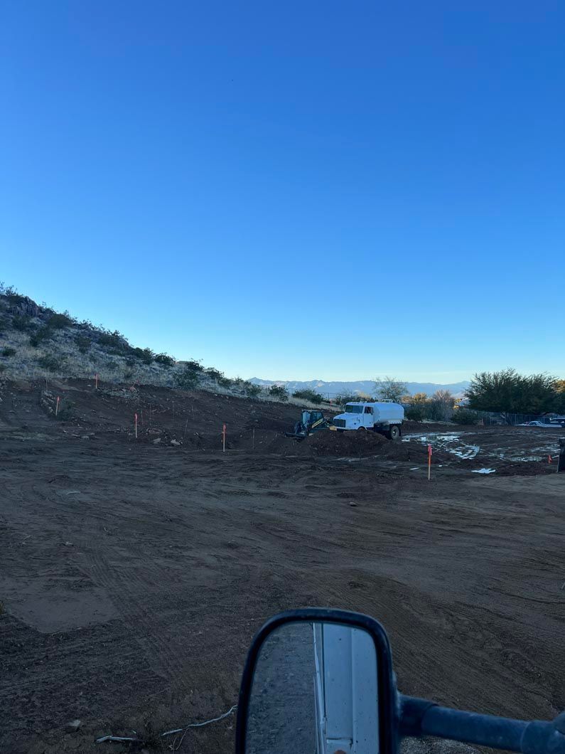 A truck is parked in a dirt field with a blue sky in the background.