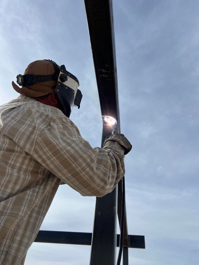 A man wearing a welding mask is welding a metal structure.