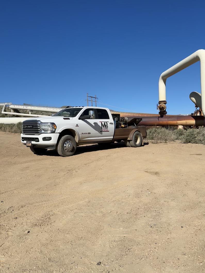 A white truck is parked in a dirt field next to a pipe.