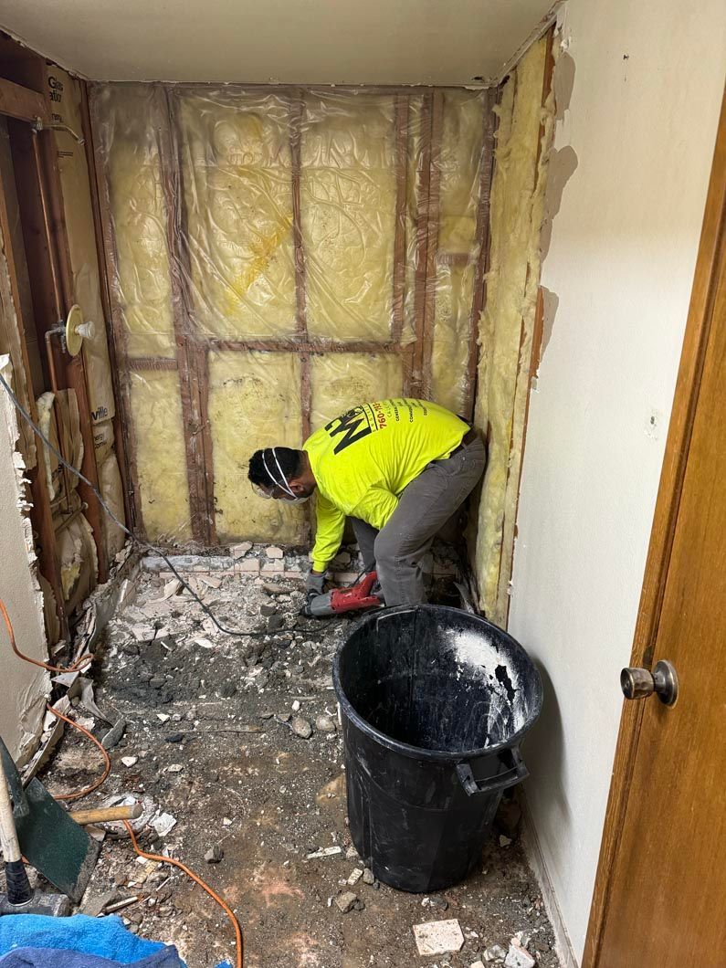 A man is kneeling down in a room next to a bucket.