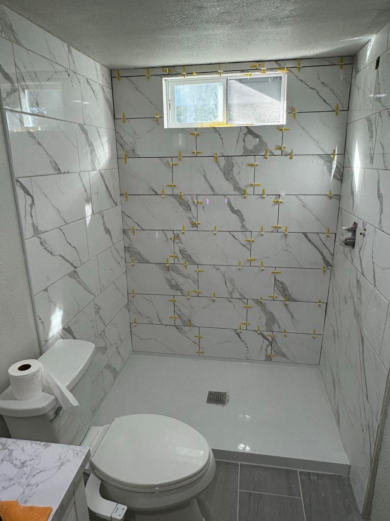 A bathroom with a toilet , sink , shower and window.