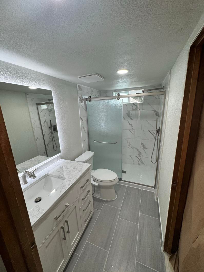 A bathroom with a sink , toilet , shower and mirror.