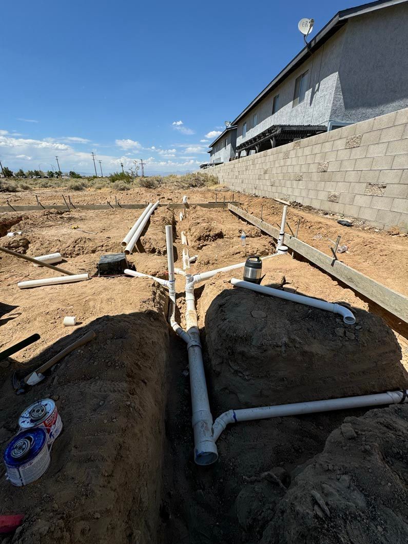 A bunch of pipes are laying in the dirt in front of a house.