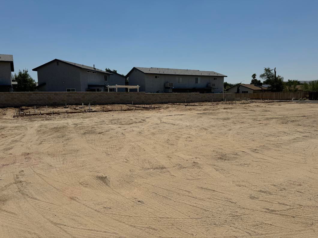 A dirt field with a fence and houses in the background.