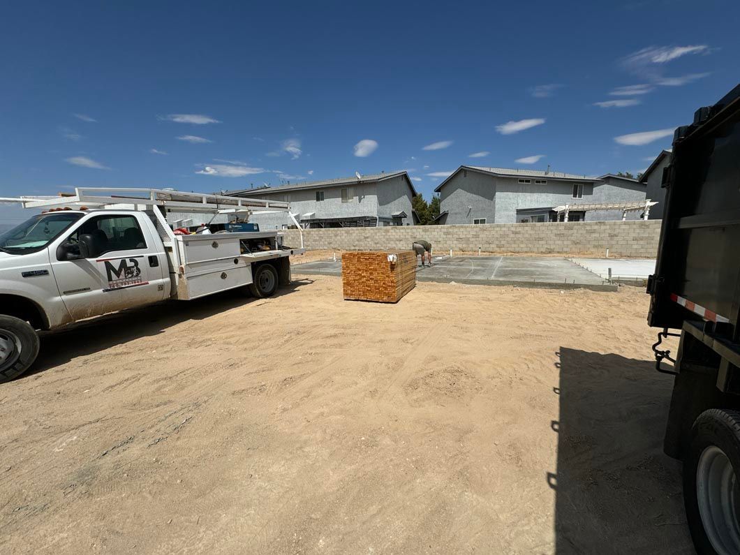 A tow truck is parked in a dirt lot next to a dump truck.