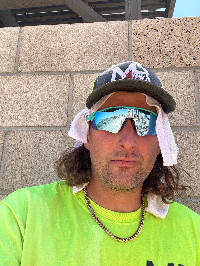 A man wearing sunglasses and a hat is standing in front of a brick wall.