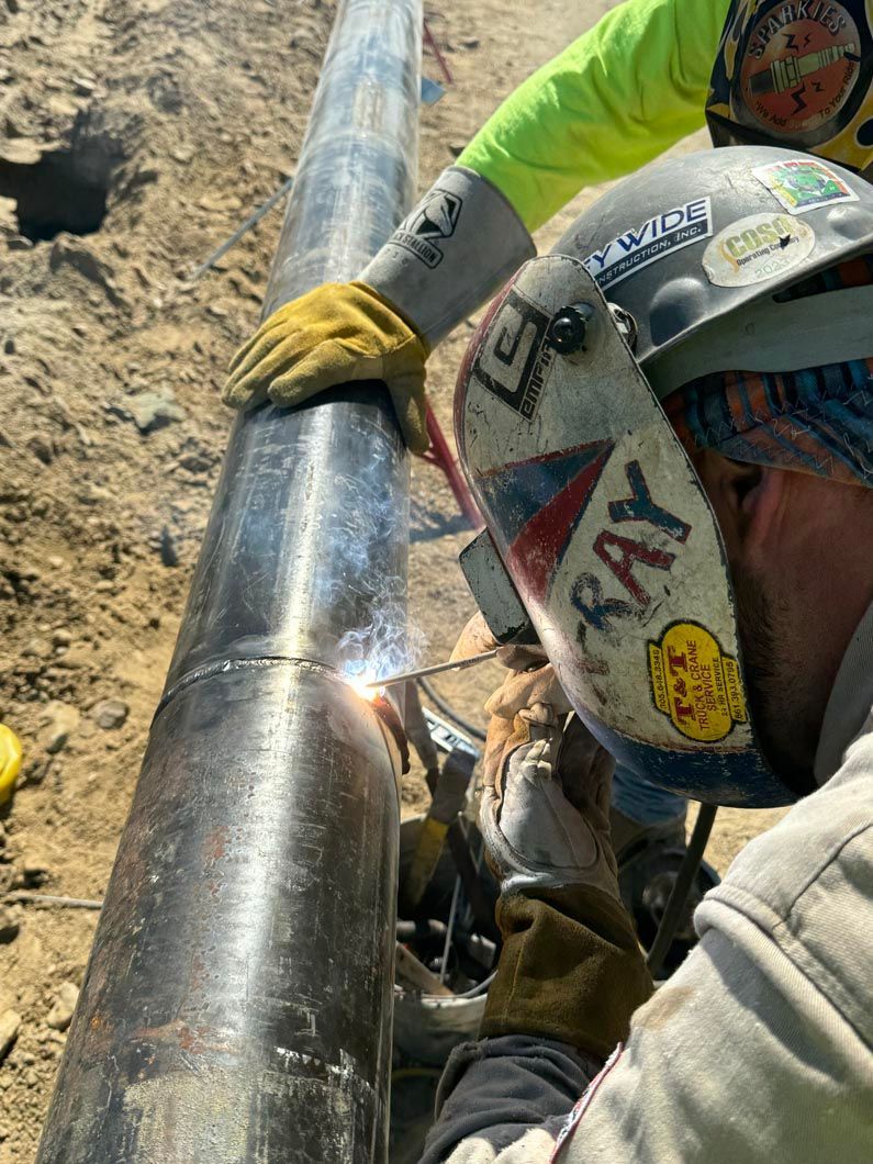 A man wearing a welding helmet is welding a pipe.