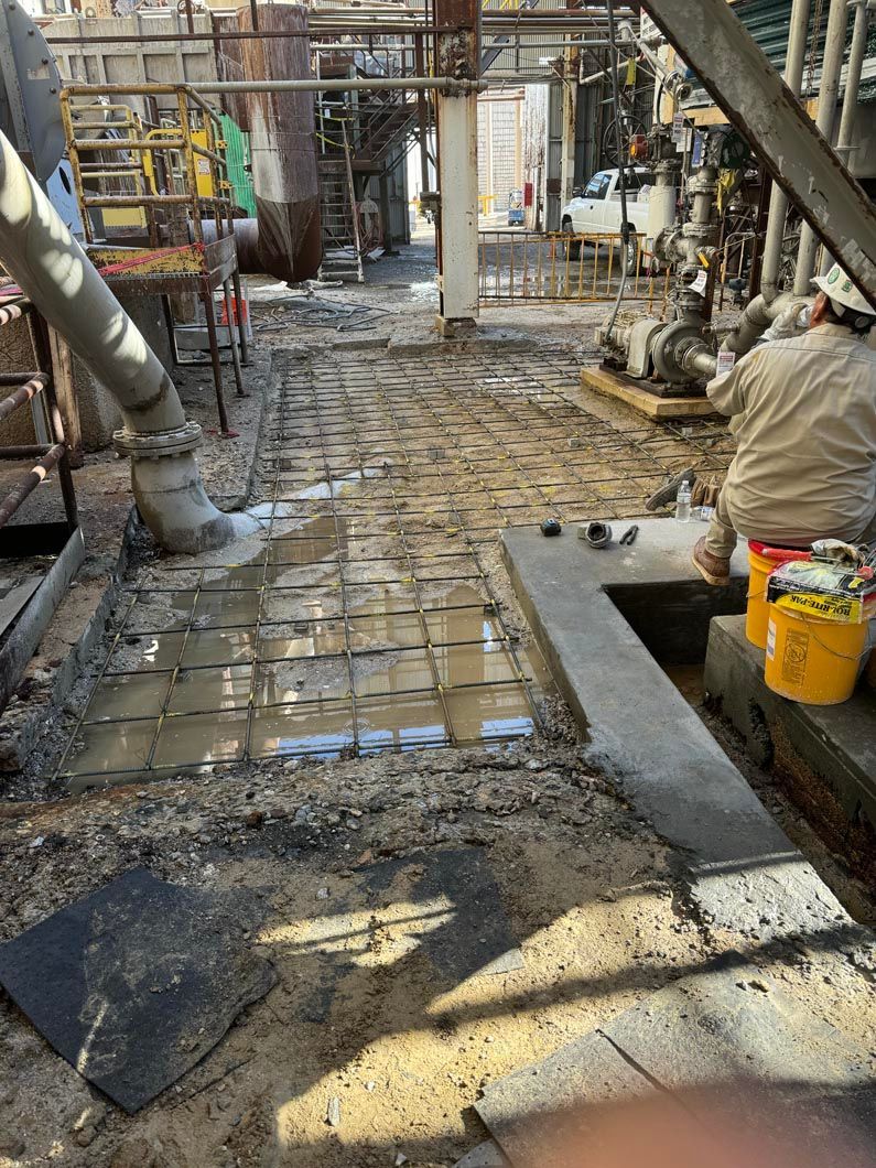 A group of construction workers are working on a concrete floor in a factory.