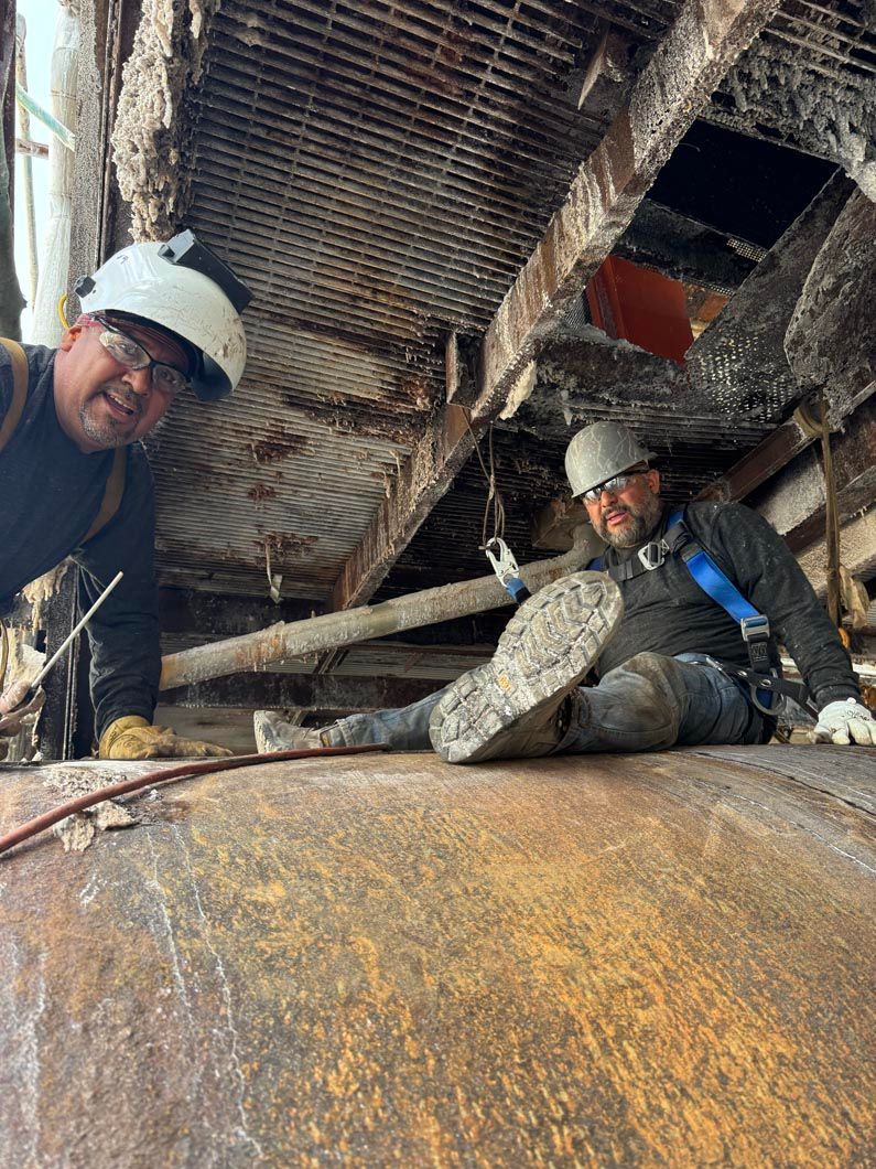 Two men are working on a large piece of metal.