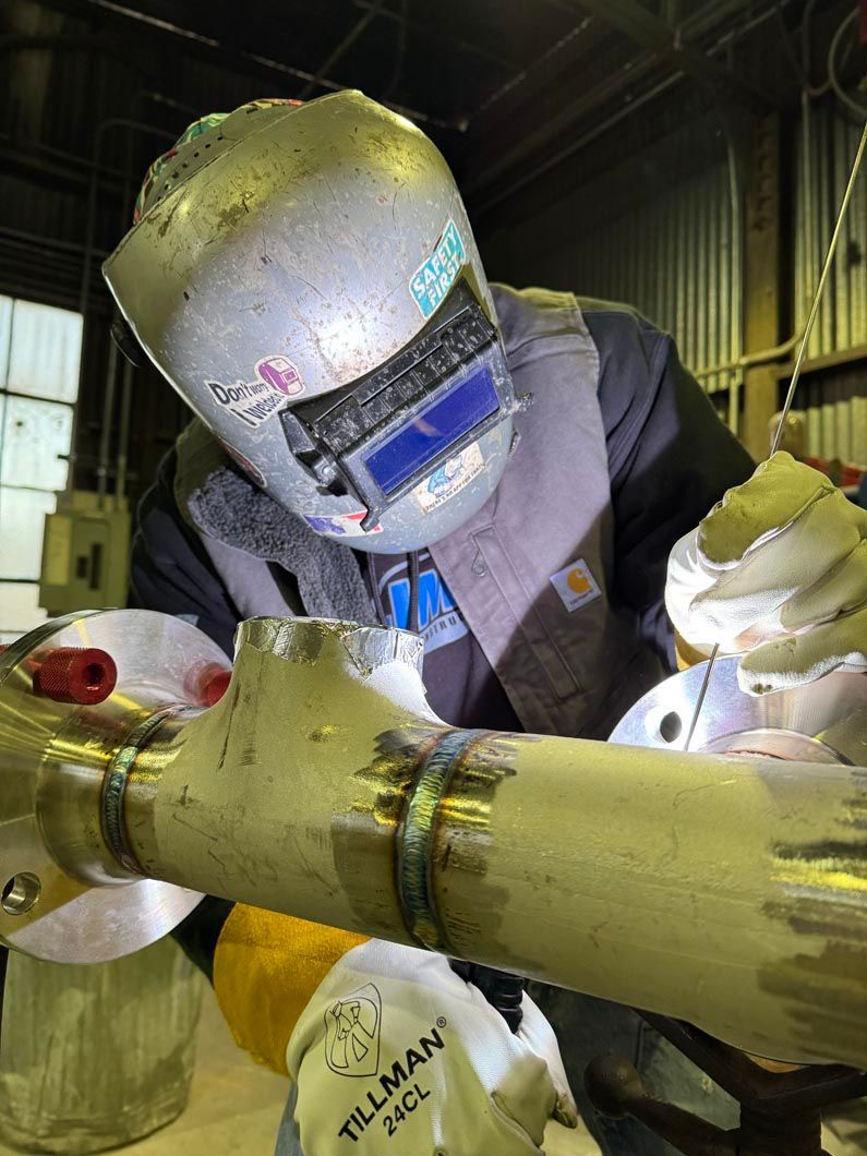 A man wearing a welding helmet is welding a pipe in a factory.