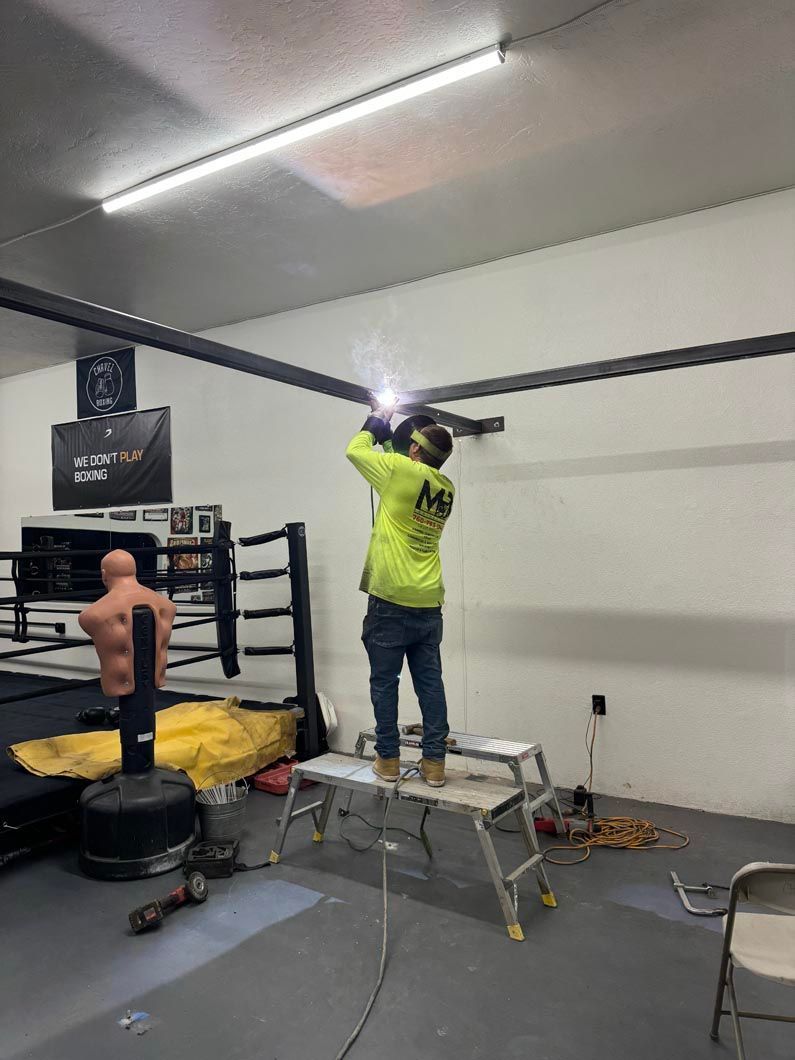 A man is welding in a gym next to a boxing ring.