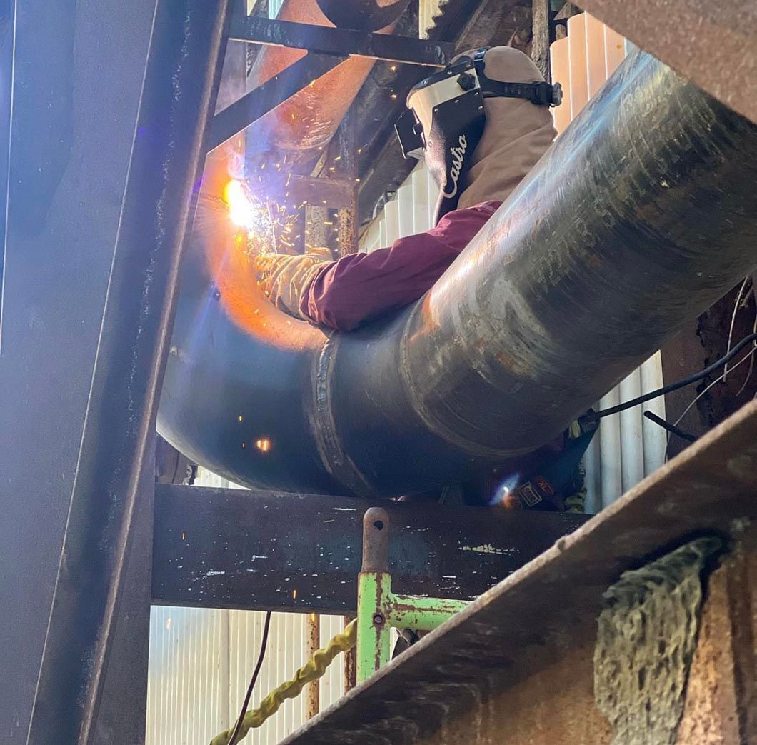 A man is welding a large pipe in a factory