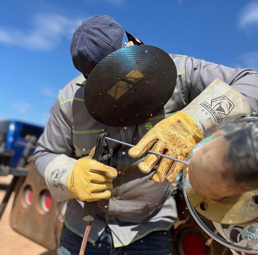 A man wearing gloves and a helmet is welding a pipe