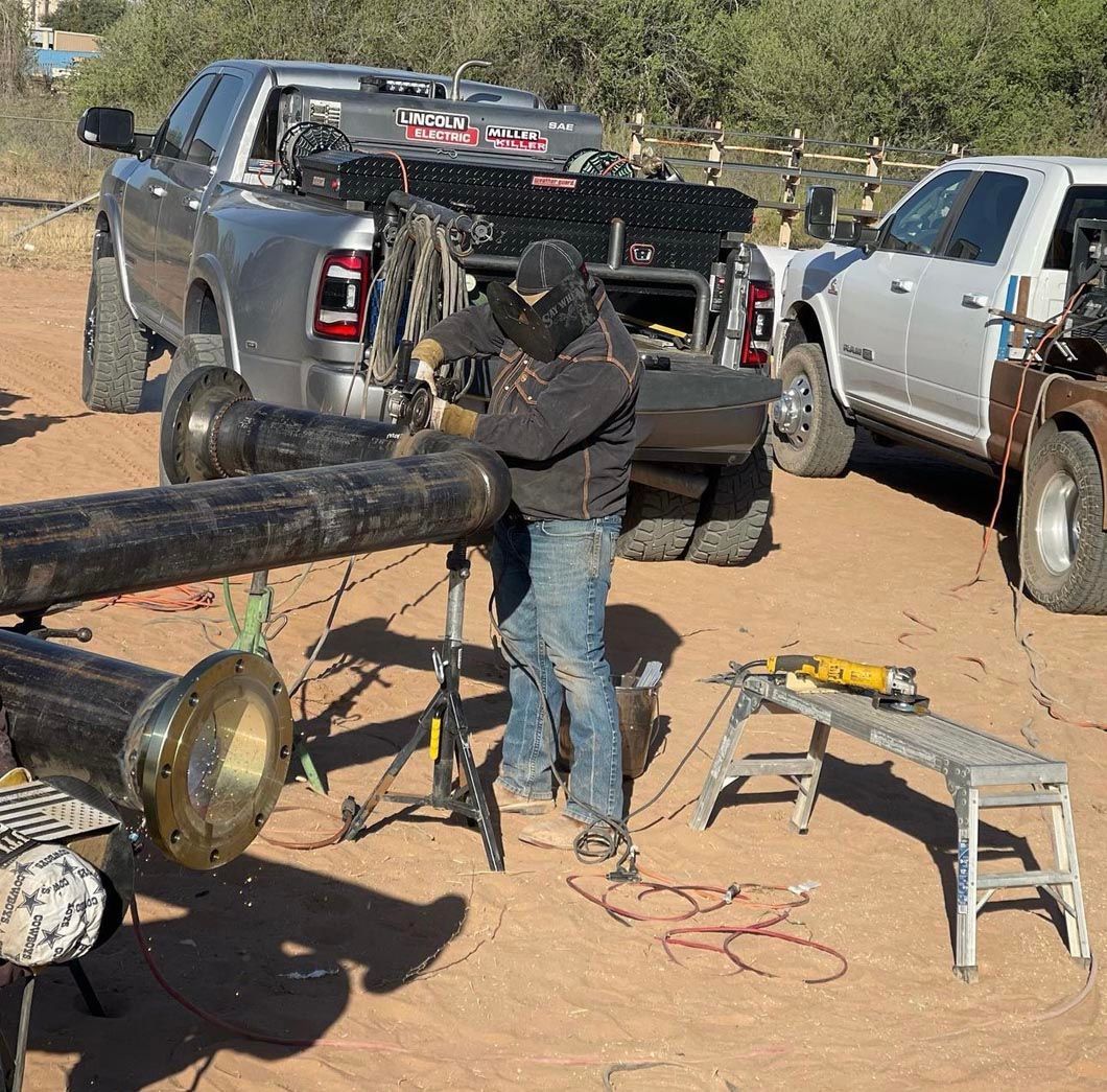 A man is welding a pipe in the dirt in front of a truck