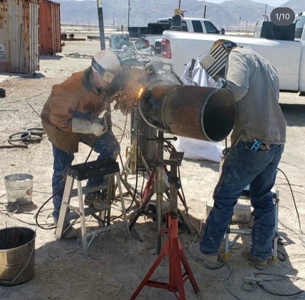 Two men are welding a large pipe in the desert
