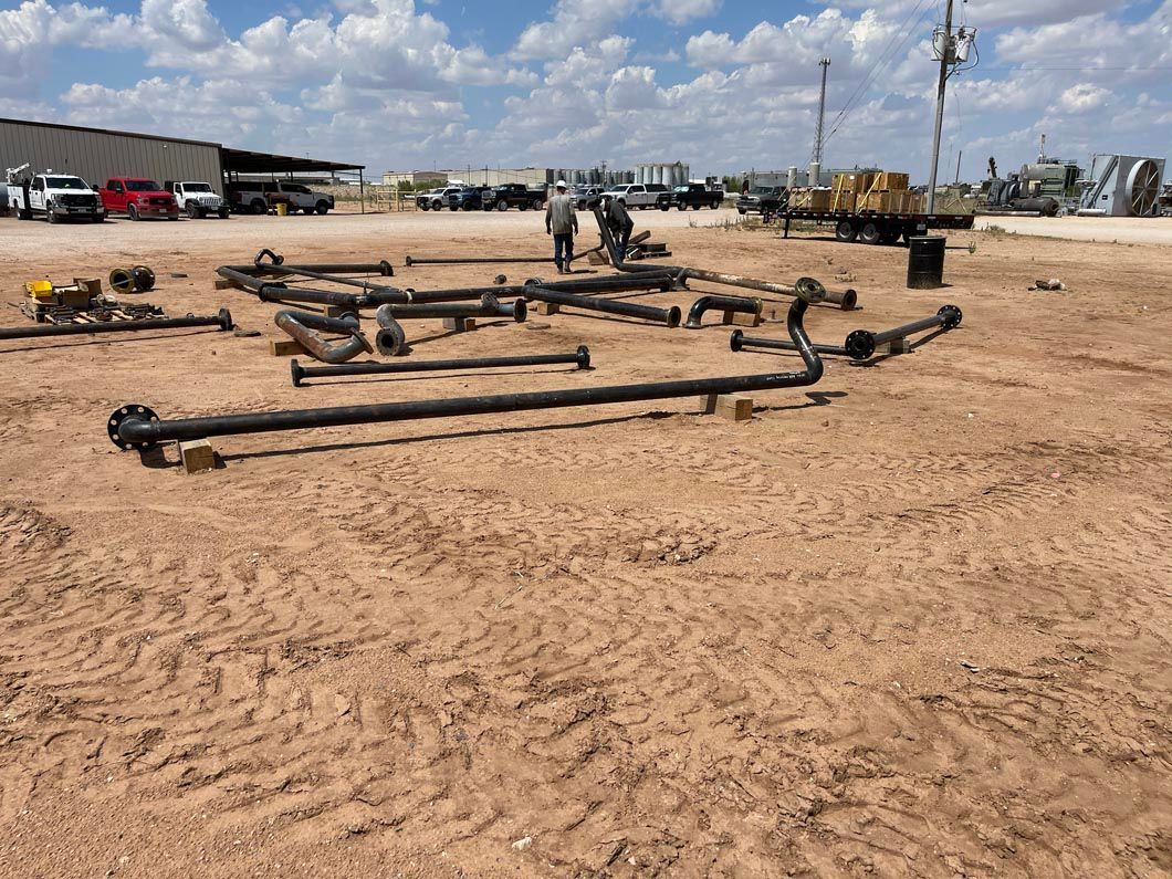 A bunch of pipes are laying on the ground in a dirt field.