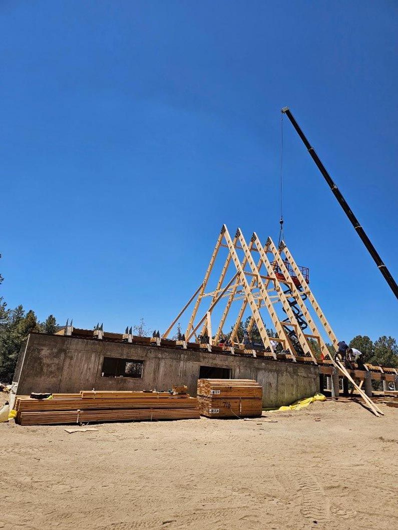 A crane is lifting a wooden structure in the middle of a dirt field.