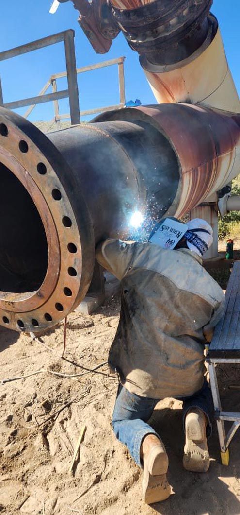 A man is welding a pipe in the dirt.