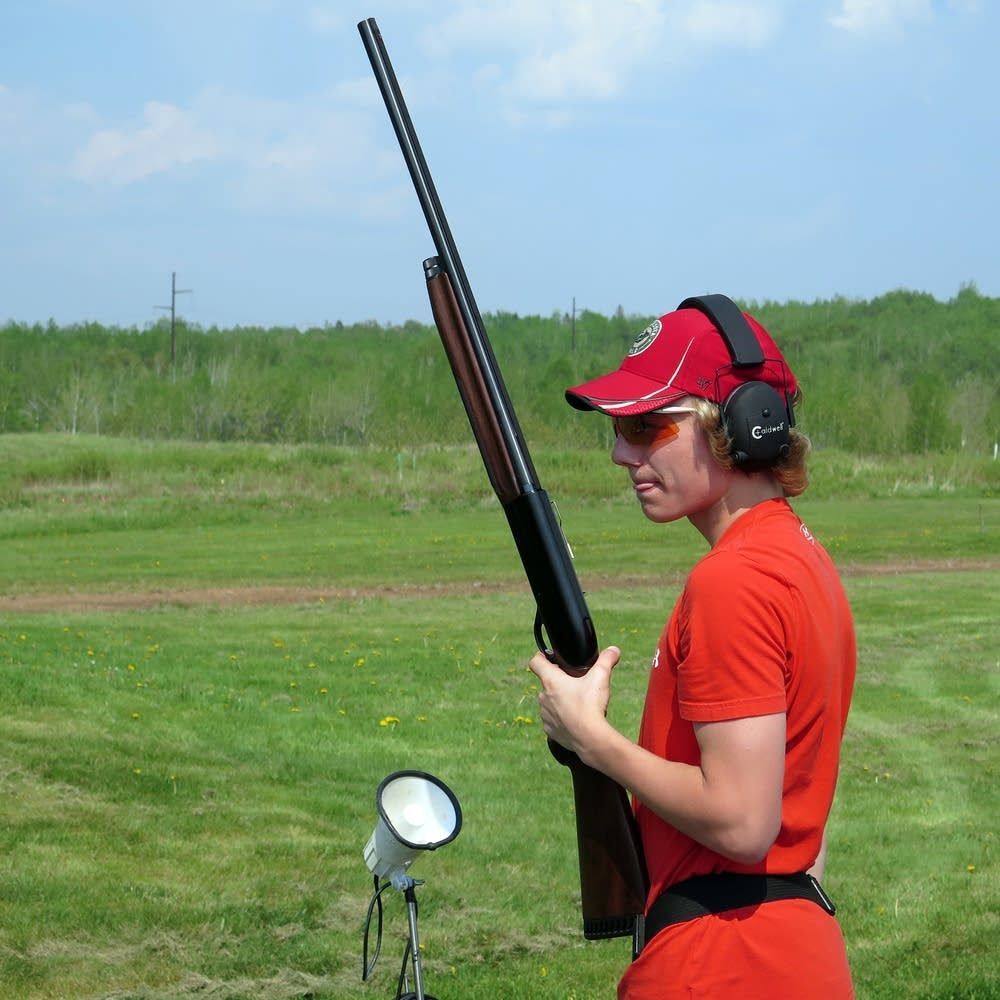 A young man is outside in a field holding a rifle for target practive