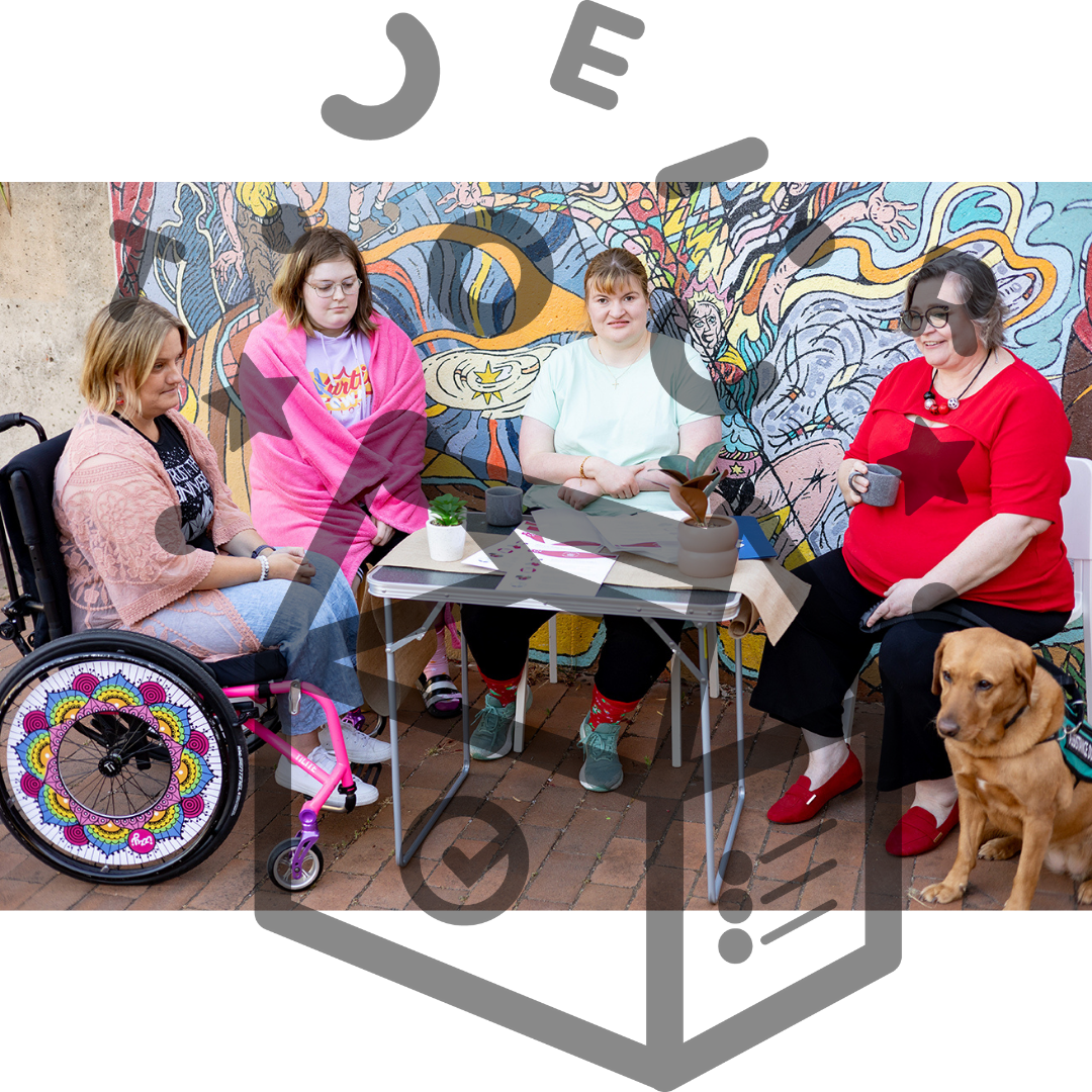 Group of 4 people sitting at a table. 1 is sitting in a wheelchair. 1 is wrapped in a blanket. 1 is sitting next to a service dog.