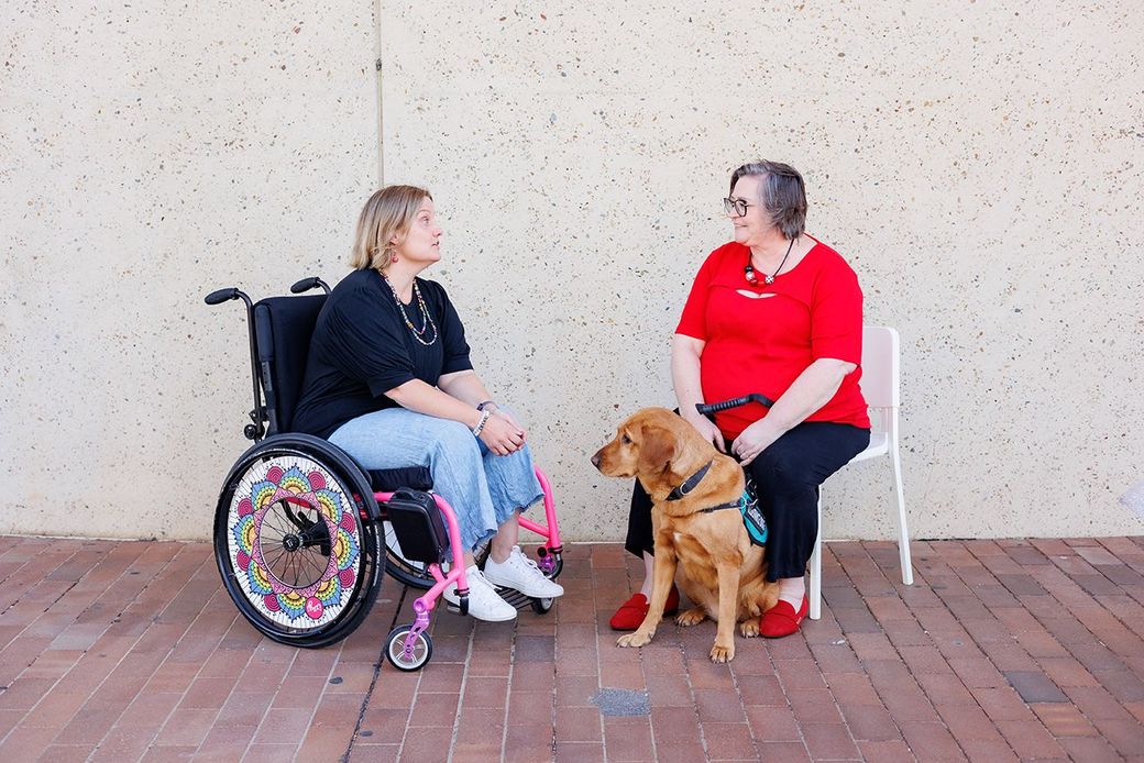 Image of a wheelchair user talking to an individual with a service dog sitting
down.